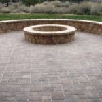 A brick patio with a fire pit and seating wall.