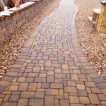 A brick walkway with a curved path leading to the side of a wall.