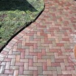 A brick walkway with grass growing in the middle.