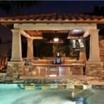 A pool with a stone wall and a large outdoor kitchen.