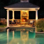 A gazebo with chairs and a fireplace next to the pool.