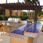 A grill and bbq are sitting under a pergola.