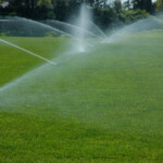 A couple of water sprinklers spraying on some grass.